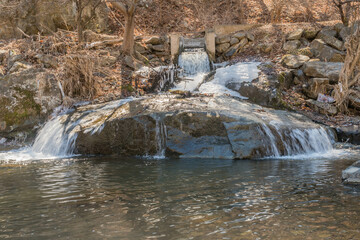 Obraz premium Winter landscape of water cascading off of large boulder into mountain river.