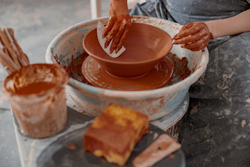 Skillful potter shaping clay bowl with instrument in art studio