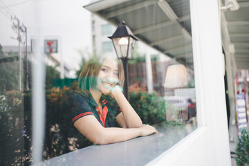 Portrait of Asian woman smiling in coffee shop cafe, shot through glass.