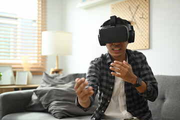 Asian man wearing virtual reality glasses playing simulation boxing game in living room.