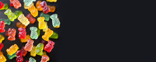 Multicolored flying gummy bears on a black background, flat lay. Banner