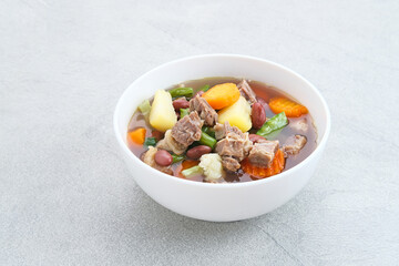 Sup daging kacang merah, clear soup with beef slices, red bean and vegetables. Served in bowl on grey background. Selected focus.
