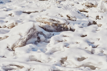 Natural texture of melting snow and ice in spring. The loose structure of snow is covered with a new fresh layer after a snowfall. Sunny day.