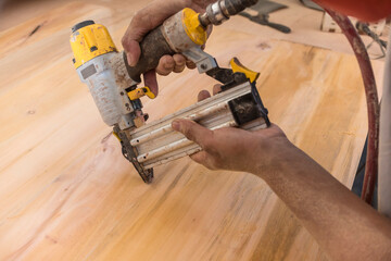 A carpenter using a pneumatic nail gun. Driving small nails into a sheet of plywood. At a furniture...