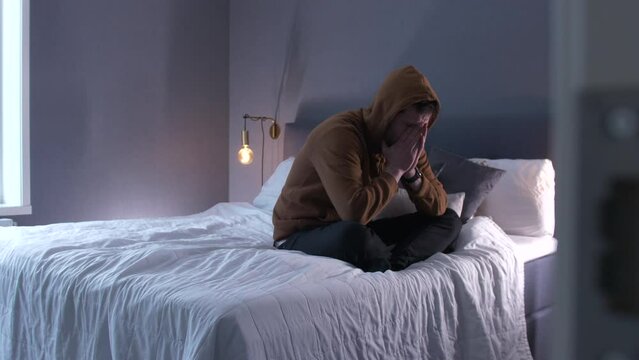 upset man sitting on the bed with legs crossed