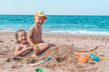 Children sister and brother lie on the beach on the sand. A girl and a little boy play in the...