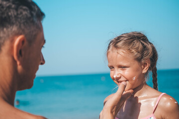 Father applying protective cream to her daughter's face at the beach. Man hand holding sunscreen lotion on baby face. Cute little girl with a sun block by the sea . Copy space.