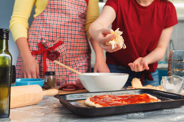 Two women make pizza. Pizza is placed on a baking sheet for sprinkling with cheese. Hands close-up. Cooking at home