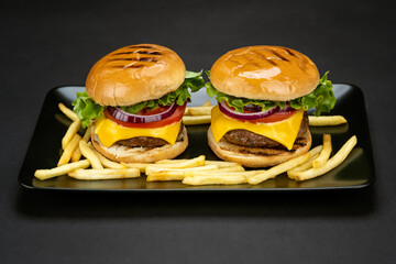 Tasty homemade beef burgers with fresh ingredients and french fries served in a black plate, close-up view.