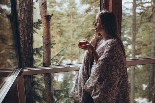 The girl drinks tea in nature. A beautiful young girl stands at the window and holds a cup of tea in her hands. High quality photo
