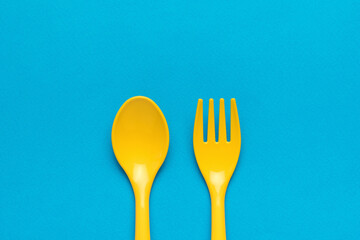 Yellow spoon and yellow fork for children close-up on a blue background. Flat lay.