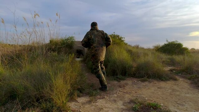 A volunteer soldier or freedom fighter takes cover in a fortified bunker as the enemy approaches at sunset