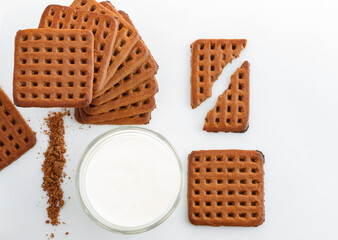 chocolate cookie laid out in geometric pattern and glass of milk on white background view from above