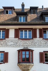 Decorative white tenement house with dark red shutters in old town in German city Würzbur, with single oriel, inscription and ornamental paintings with leaves, rabbits and wild pigs 