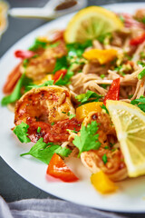Stir fry noodle with shrimps, lemon and fresh parsley on white plate, soba with prawns, asian cuisine, top view