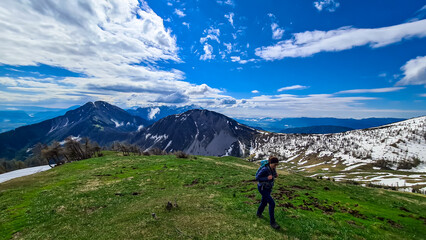 Active woman hiking on Frauenkogel with scenic view on mountain peaks in the Karawanks, Carinthia, Austria. Border with Slovenia. Triglav National Park. Kahlkogel (Golica).Snow field melting in spring