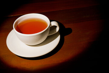 A cup of refreshing black tea, warm soft light, dark wood background.