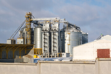 agro silos granary elevator in winter day in snowy field. Silos on agro-processing manufacturing plant for processing drying cleaning and storage of agricultural products, flour, cereals and grain.