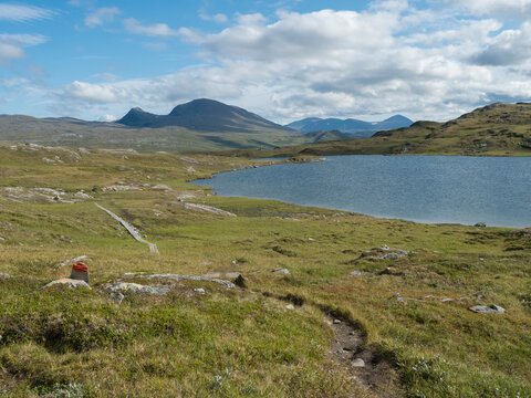 Beatiful northern landscape, tundra in Swedish Lapland with blue artic lake, green hills and mountains at Padjelantaleden hiking trail. Summer day, blue sky, white clouds
