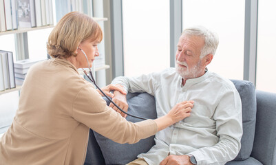 Doctor talking with her patient. Health visitor and a senior man during home visit. Doctor or nurse with stethoscope visiting senior man and checking her breath or heartbeat at home
