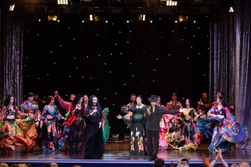 A collective of musicians, singers and dancers in gypsy costumes perform on stage.