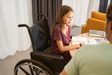 Girl in a wheelchair is studying with an adult male