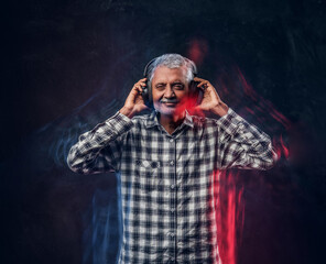 Cheerful old man with headphones dressed in plaid shirt