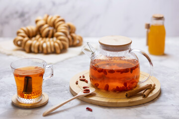 Glass teapot with hot tea with goji berries, a jar of honey and cinnamon sticks on a bamboo stand. Selective focus.