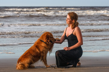 smiling young woman playing with her dog on the beach