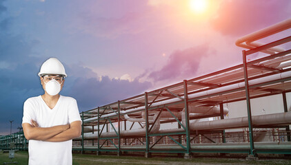 Industrial technician wearing N95 face mask standing in front of petrochemical pipeline at industrial zone.