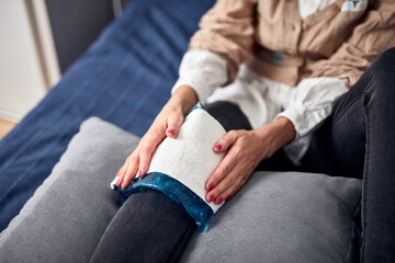 Fototapeta premium Woman with spasm, cramp, sprained, dislocated knee, ruptured tendon and joint pain, using cold gel pack at home.