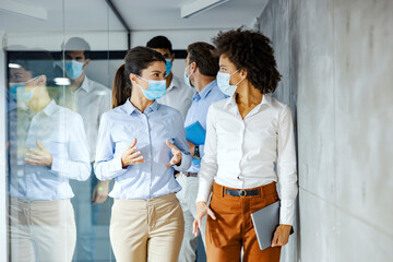 A multicultural group of business people with face masks walking and discussing about the project.