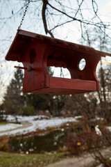 Red wooden birdhouse hanging on a tree branch.