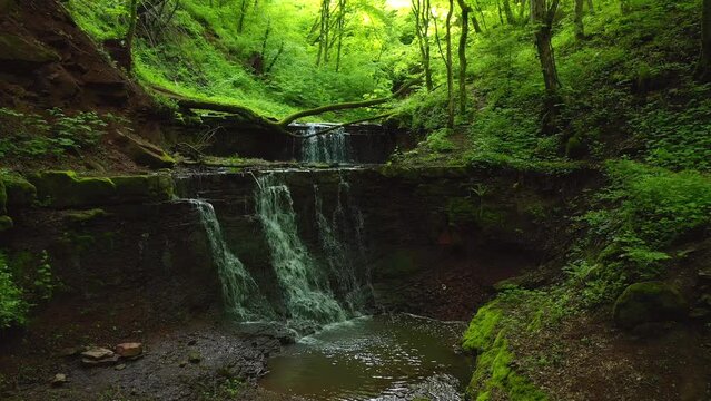 A quadcopter flies in a wooded green canyon over an exotic waterfall. Filmed in UHD 4k video.