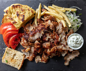 Greek gyro traditional meat food on black, overhead. Ethnic dish, meat cut, pita bread and tzatziki