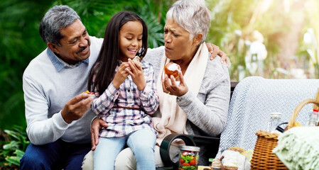 We always have healthy treats for her. Shot of a cheerful little girl sitting down on a bench with her grandparents at the park.