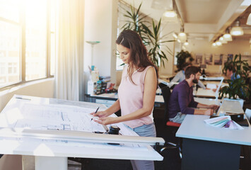 Working on a new building plan. Cropped shot of a young architect working on her drafting table.
