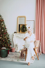 Beautiful young woman in a carnival rabbit mask and white costume celebrates the new year near the Christmas tree in a modern interior. Inspiration. Soft selective focus.