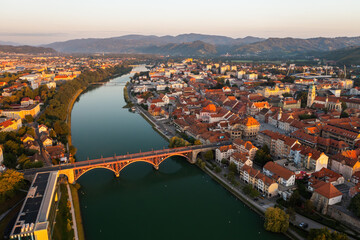 Obraz premium City of Maribor in Slovenia illuminated by rising sun in the summer morning. Lovely town with river flowing in the middle from aerial perspective. Touristic destination from above.