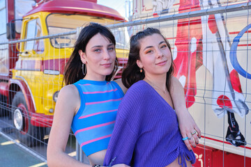 Two friends looking to the camera standing in the street next to a circus parade