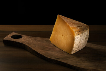 Chunk of a Kars cheese on a wooden cutting board and black background