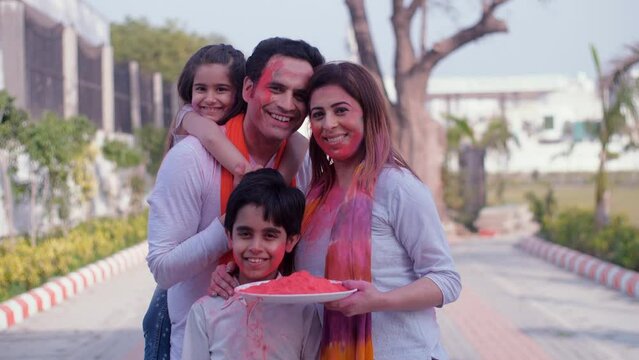 A beautiful woman with her husband and kids on Holi - posing for camera  Holi celebrations  organic Gulal  vibrant colors. A cheerful modern family with their faces smeared with Holi colors - festi...