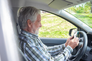 Senior caucasian man stops driving the car to unswer phone. Smiling bearded elderly grandfather holding smart phone in hands