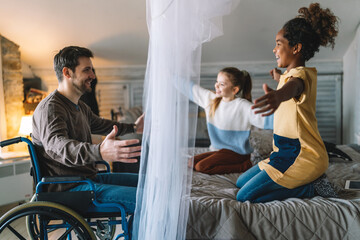Fototapeta premium Happy family. Smiling father with disability in wheelchair hugging with children at home
