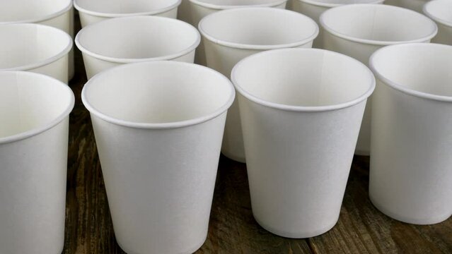 Row of white disposable paper cup for coffee or hot beverage on dark backdrop rotate slowly.