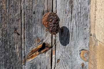 Vieille poignée de porte sculptée et rouillée sur une vieille porte d'entrée en bois d’accès à un jardin dans un petit village auvergnat