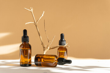 Facial serum, in three amber glass bottles with dropper lid on beige background with floral shadow....