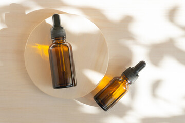 Facial serum in amber glass bottles with dropper lids on round wooden stand. Flat lay, white...