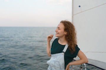 Smiling young red-haired woman on a yacht looking away in the middle of the sea