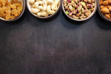 Various varieties of nuts and dried fruits are in a bowls on black background. Top view. Healthy food. Vegetarian nutrition. cashew, almond, pistachio, and raisins. Assorted nuts banner. Copy space